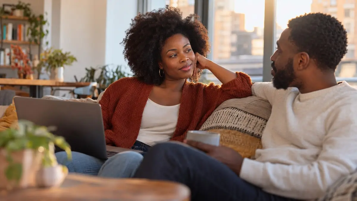 Une femme noire échange un regard chaleureux avec son partenaire dans un salon lumineux.